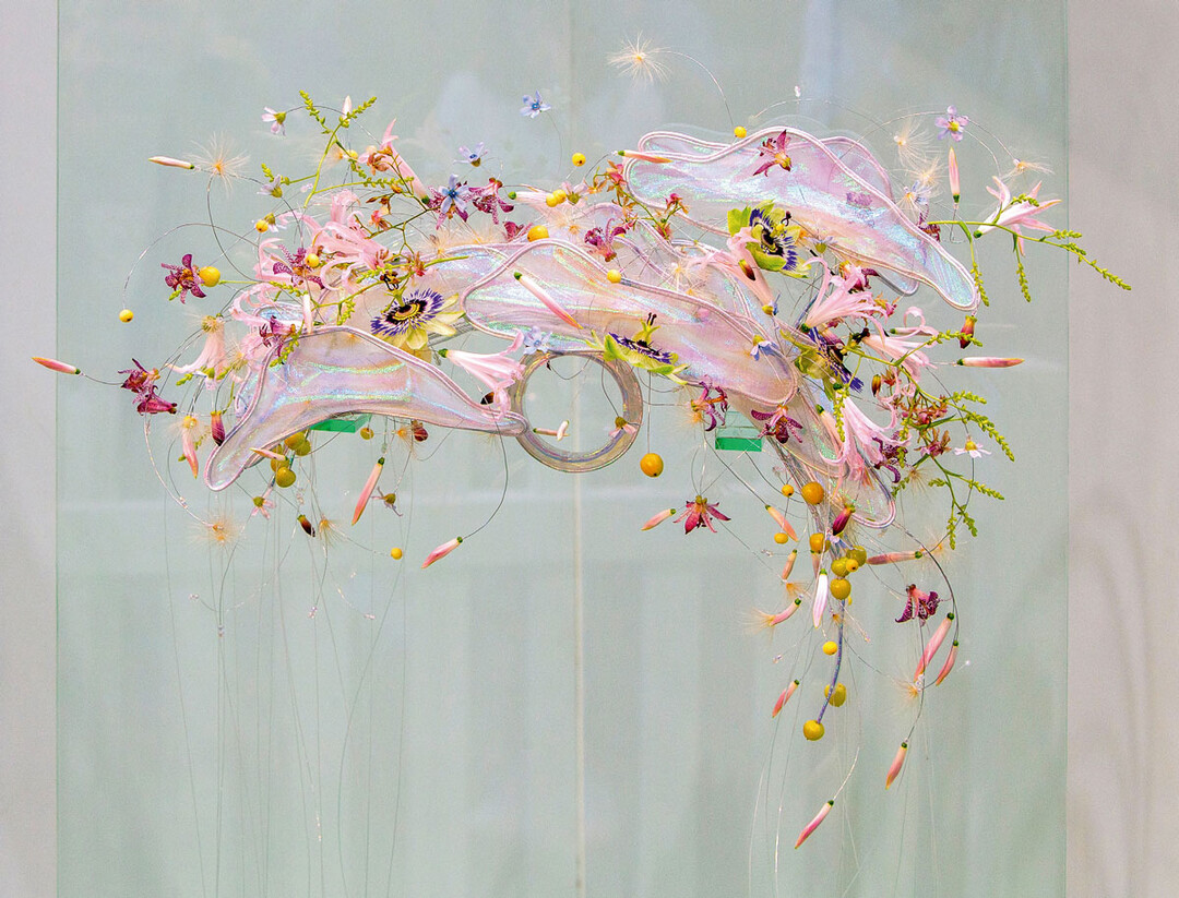 Die Elemente sind holografisch, was dem Werkst�ck zu besonderem Glanz verhilft. Die Bl�ten sind einzeln auf Draht gef�delt und schweben um die Elemente. Der Schmuck ist auf beiden Seiten abflie�end und wirkt wie ein Brautschmuck der Zukunft oder aus einer anderen Dimension. Die Leichtigkeit, die Elizabeth Newcombe hier pr�sentiert, macht neugierig auf mehr Floristik dieser Art.