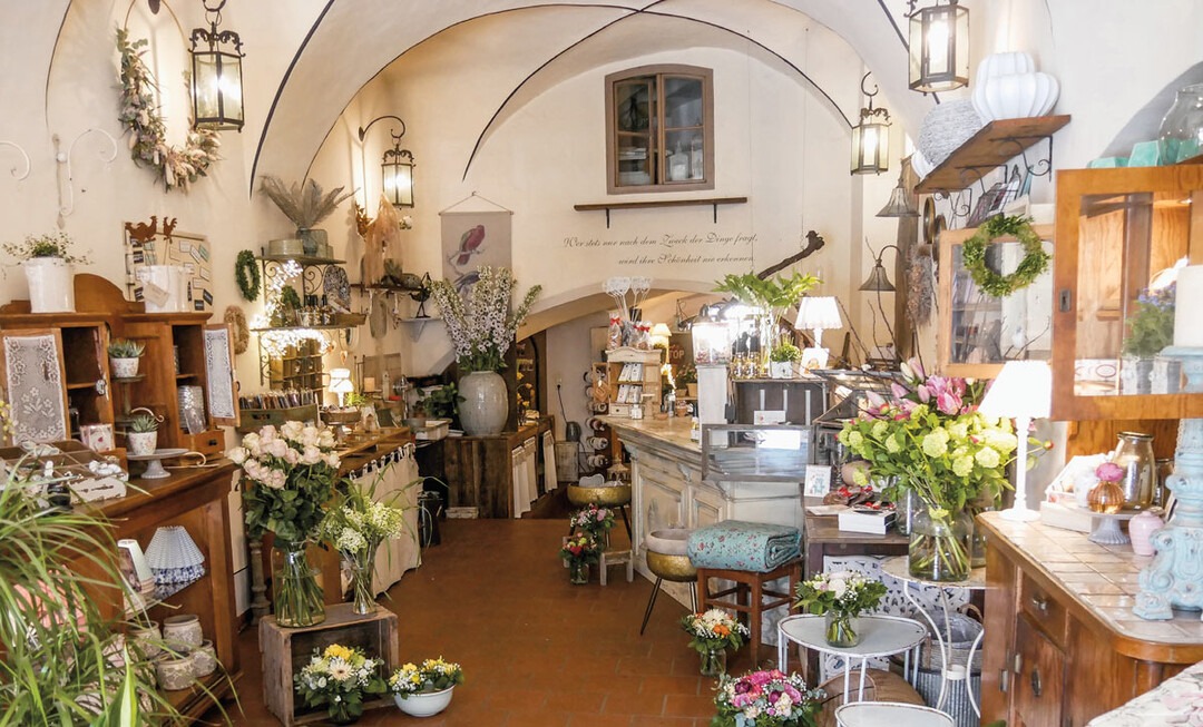 2) Regale, Schränke, Sideboards stehen an den Wänden, alle dekoriert mit Geschirr, Lampen, Seifen, Schmuck, Schokoladen, Lesebrillen, aber natürlich auch vielen Blumenarrangements, die über die Fläche verteilt sind: mal als fertige Aufträge, die auf ihre Kunden warten, mal als kreative Idee, spielerisch leicht und wahre Hingucker.