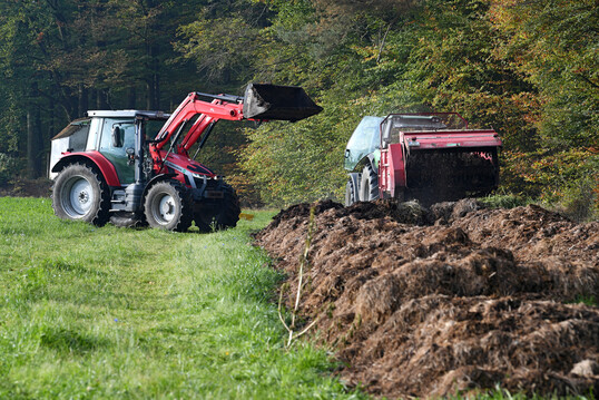Eine Kompostmiete aus Landschaftspflegegras wird mit Radlader und Miststreuer gewendet, um spter als Dnger aufgebracht zu werden.